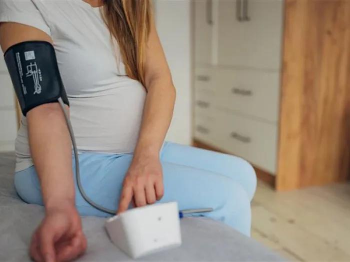 woman taking her blood pressure on bed while pregnant