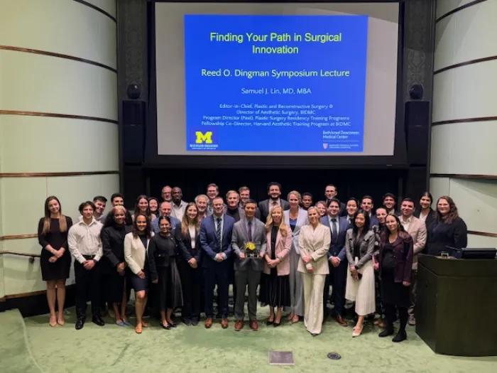 A group of people standing on a lecture hall stage in business attire. A slide behind them reads "Finding your path in surgical innovation."