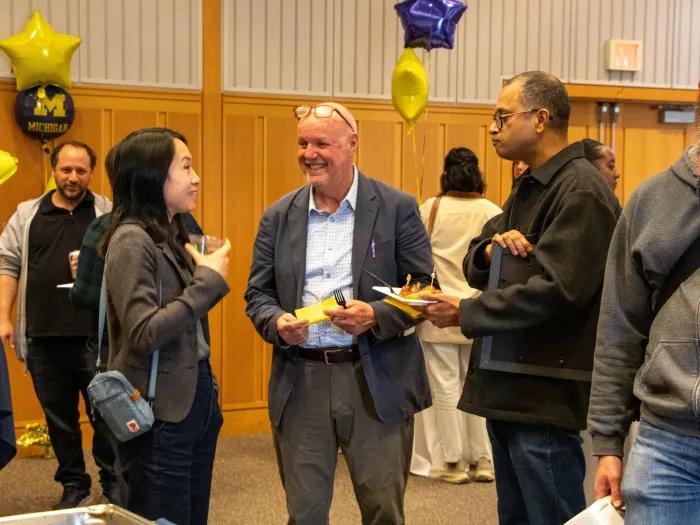 Several people stand and talk, holding plates of food