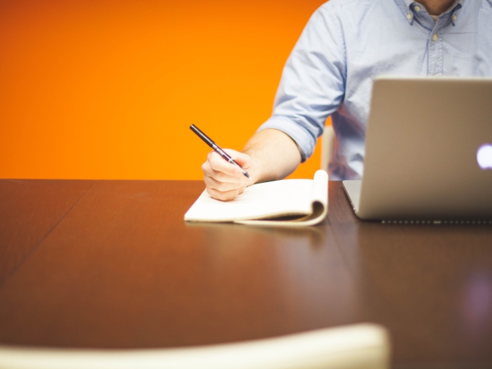 person taking notes in front of a laptop