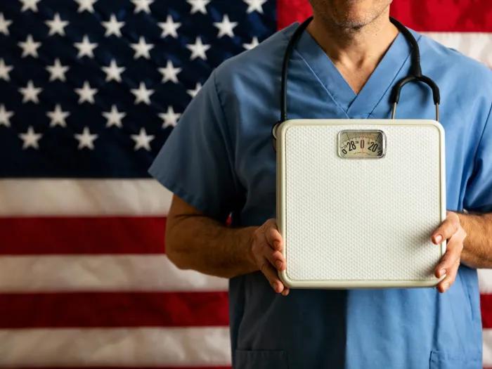 person holding scale with scrubs on and stethoscope 