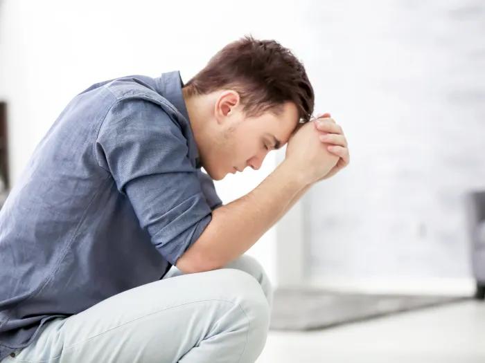 A man sits with his head against clasped hands as if in deep thought