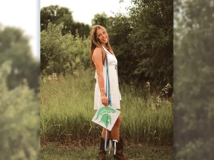 girl smiling with graduation cap in white dress field behind her