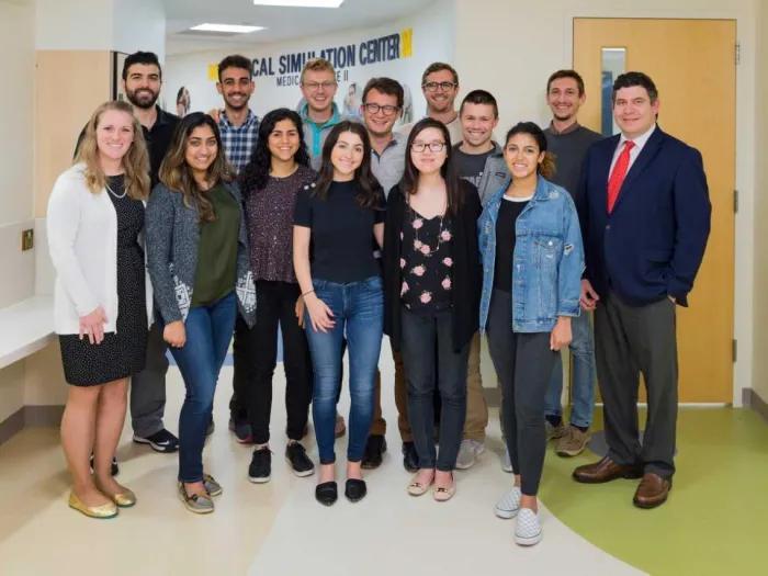 Fourteen people pose together in a hallway outside the University of Michigan Medical School's Clincial Simulation Center.