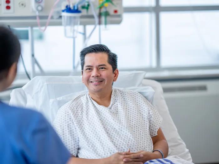 A hepatology patient sitting up in a hospital bed talks with a health care professional.