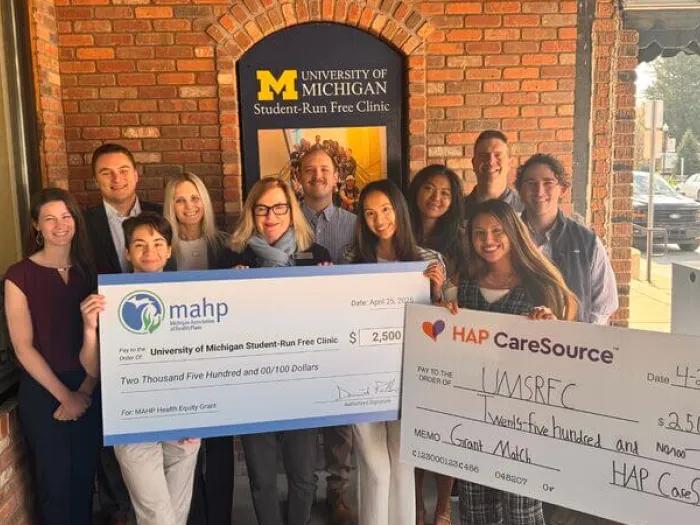A group of volunteers and supporters outside the University of Michigan Student-Run Free Clinic holds two ceremonial $2,500 donation checks from MAHP and HAP CareSource.
