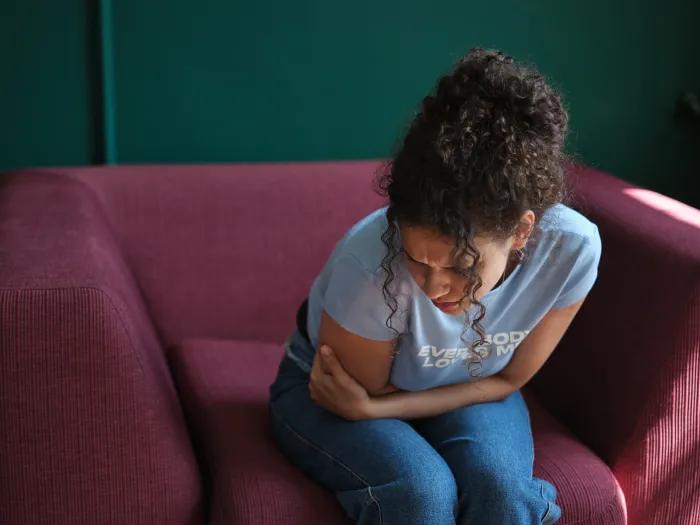 getty image of a woman bending over in a red seat in pain with green painted background