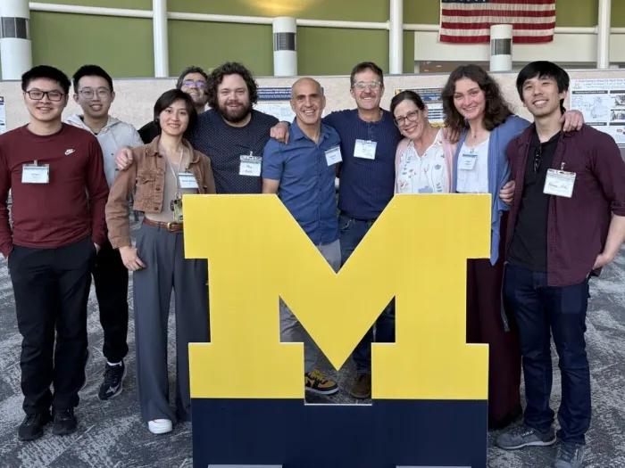 Kamran Diba and his lab members pose for a group photo behind a large block M