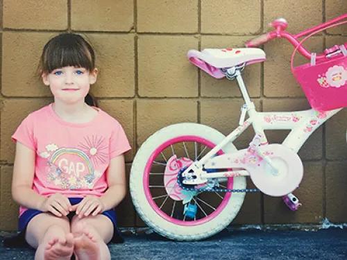 Artistic photograph taken by Dr. Rosen of a young girl sitting against a wall next to a pink bicycle