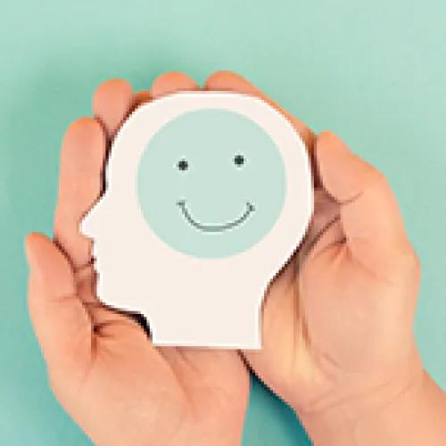 Hands holding a cutout of a head with a smiley-face brain