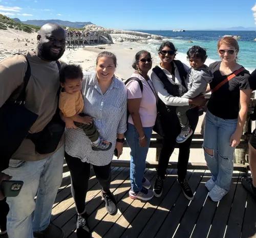 A group of adults and young children posing together on a sunny wooden boardwalk