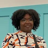 Black woman with dark hair, glasses, and an orange and black top