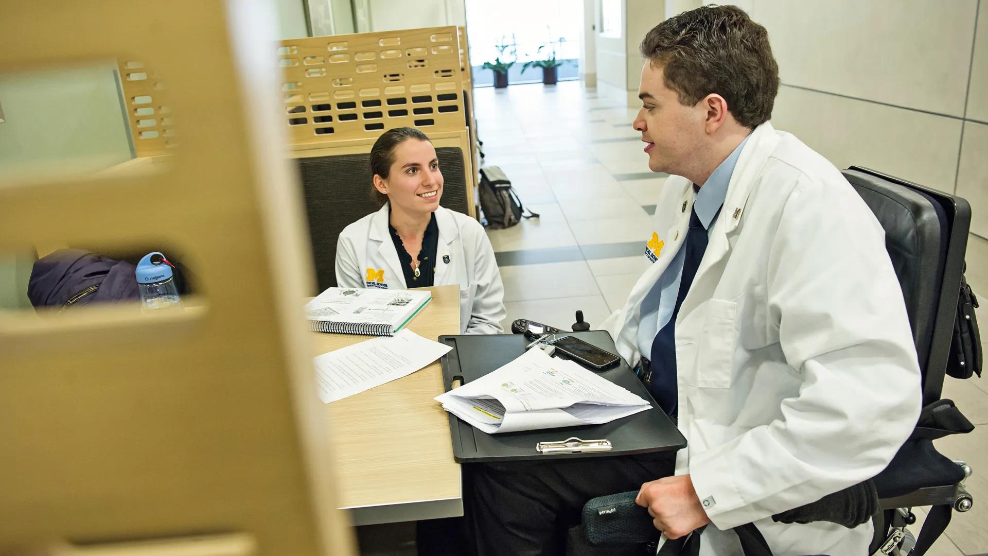 Young female doctor seated and smiling across from young male doctor in a wheelchair