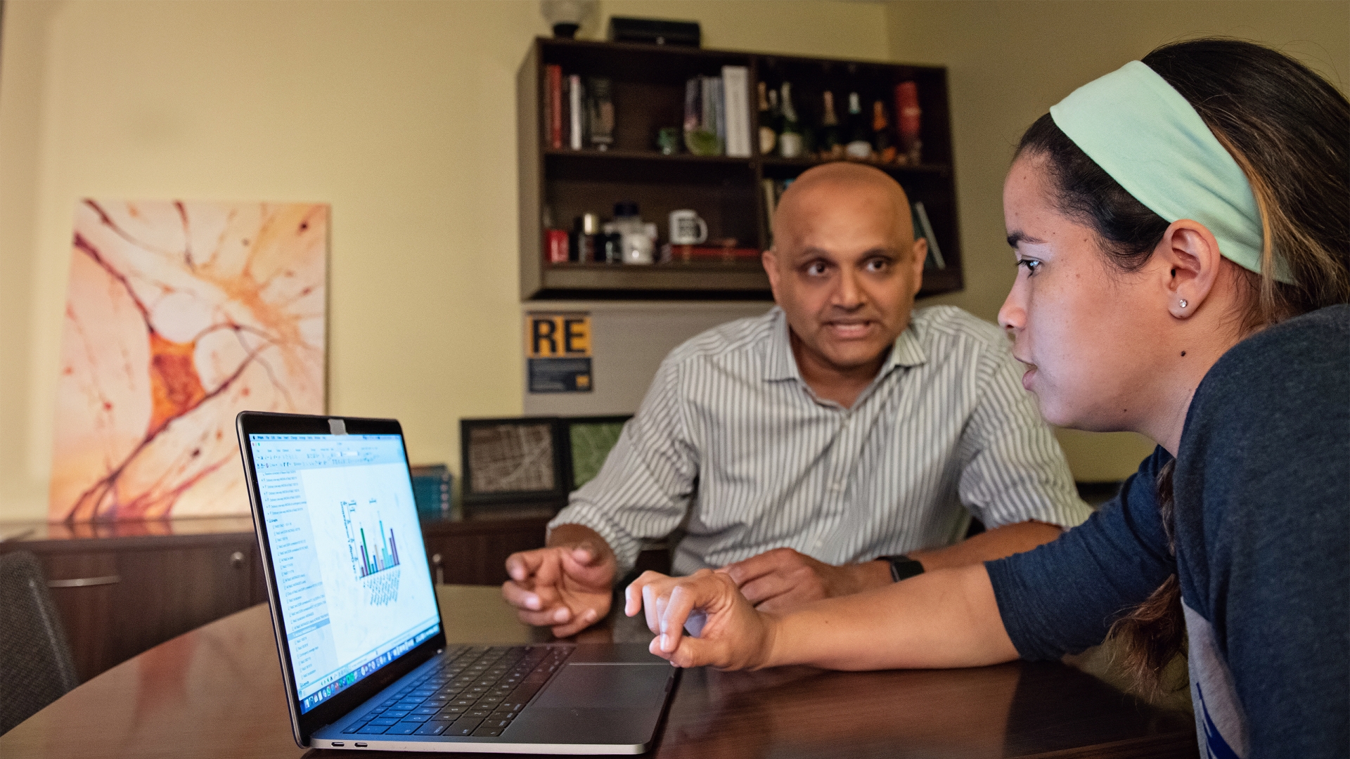 Brown-skinned man and female student in front of laptop showing a graph