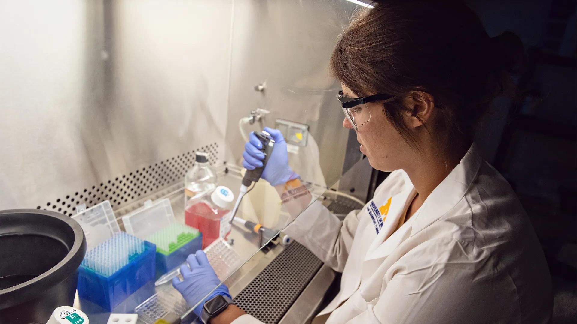 Female researcher wearing white medical jacket and blue surgical gloves working in lab