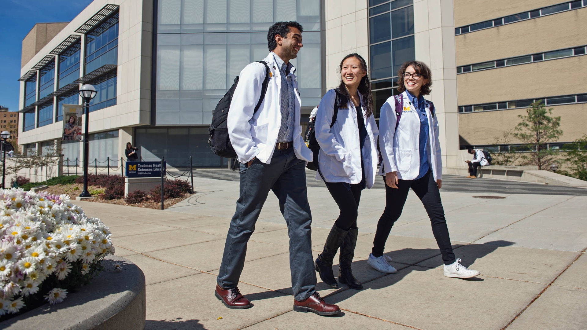 Three people walking outside a Michigan campus building