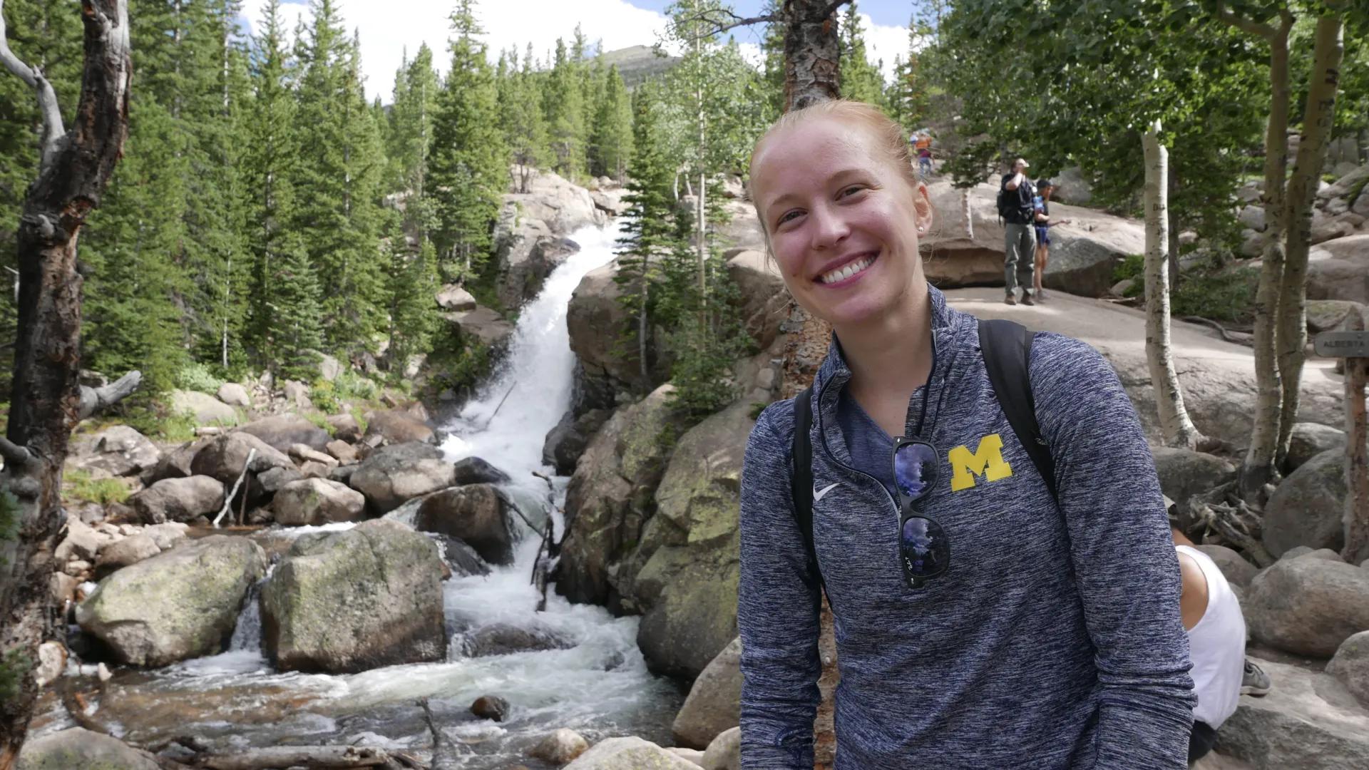 A student hiking through the forest near a waterfall