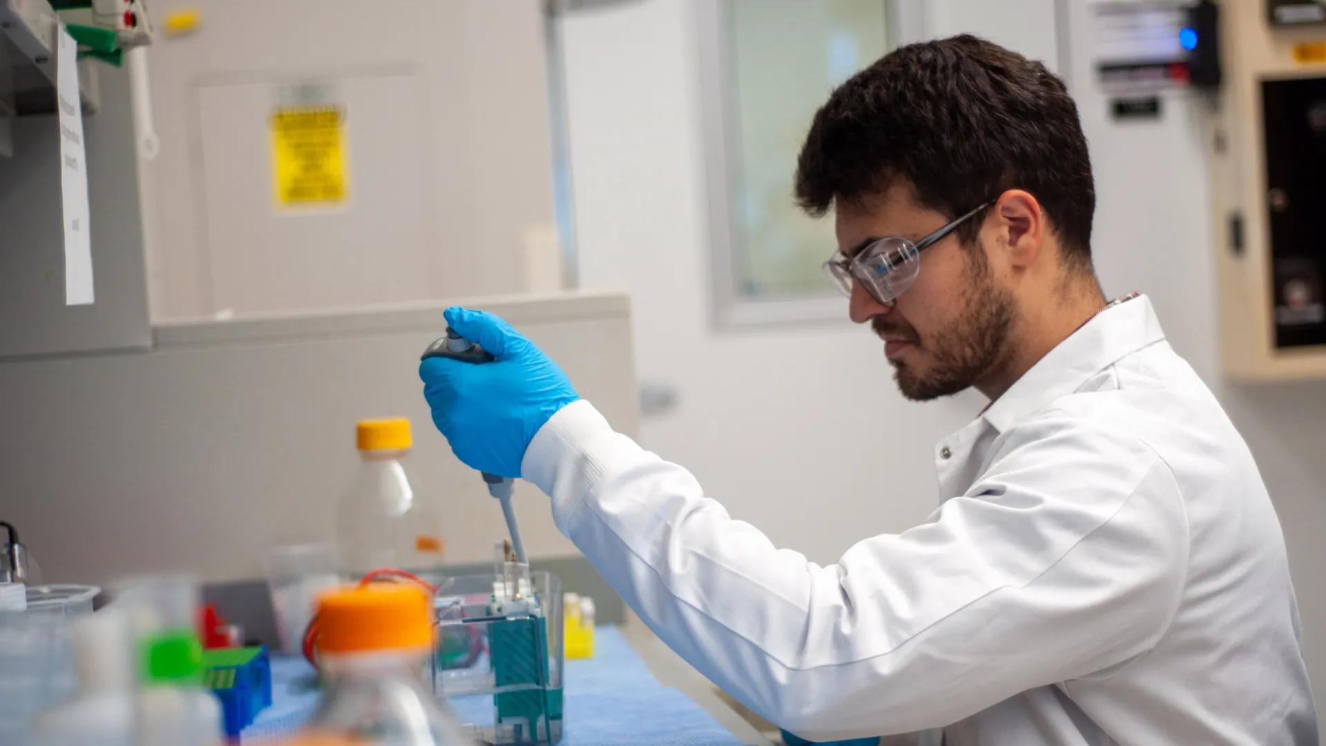 Researcher in a lab coat using a pipette at a laboratory bench.
