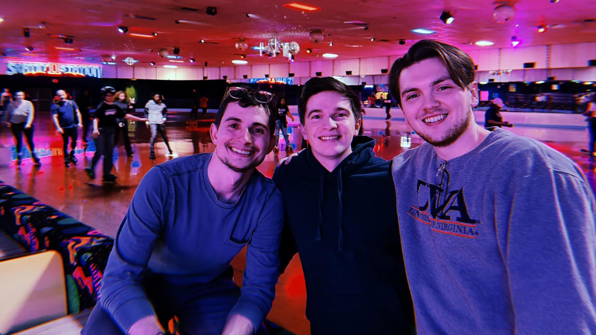 Three friends pose together at an indoor roller-skating rink with colorful neon lighting, while other skaters move around in the background.