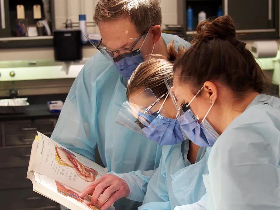 lab students and professor in gear reading textbook