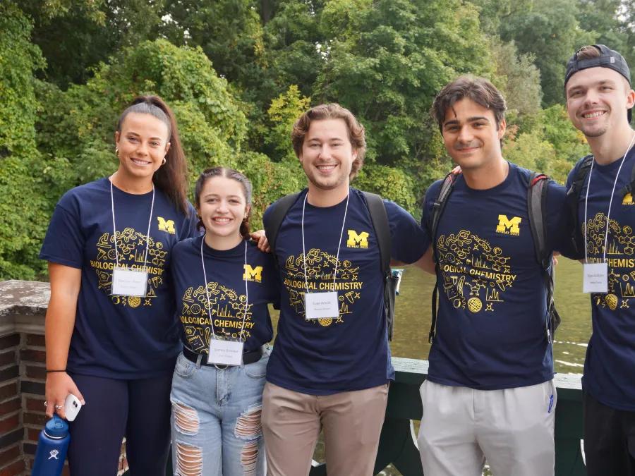 five bio chem students stand in front of water on bridge 