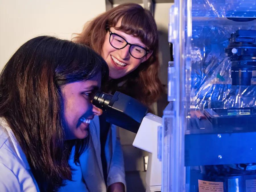 Two people smiling working with a microscope