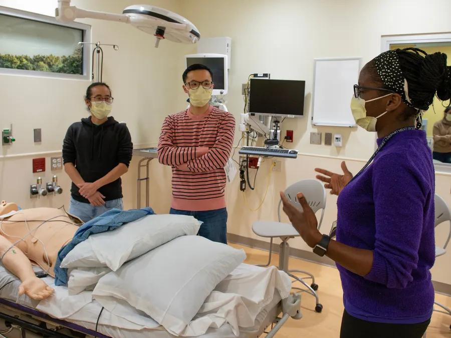 faculty demonstrating students about a dummy lying in hospital bed