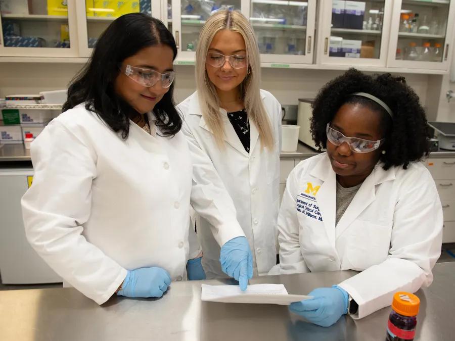 group photo of three women in lab looking at paper 