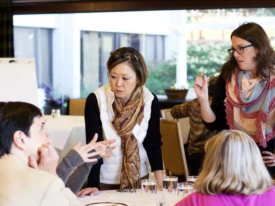 Photo of 5 women focused on a project on a table.