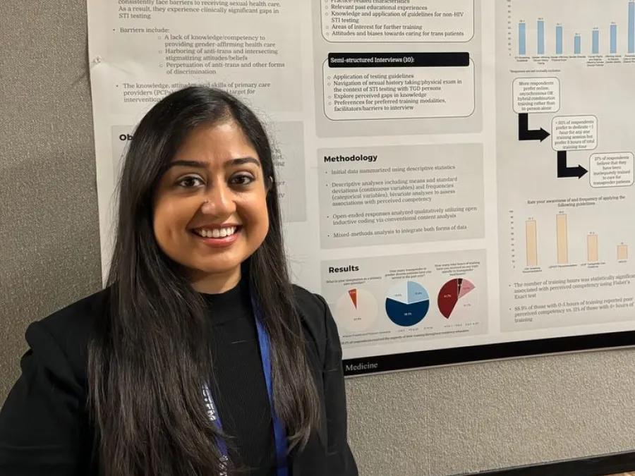 family medicine fellow smiling and standing in front of her presentation at a conference