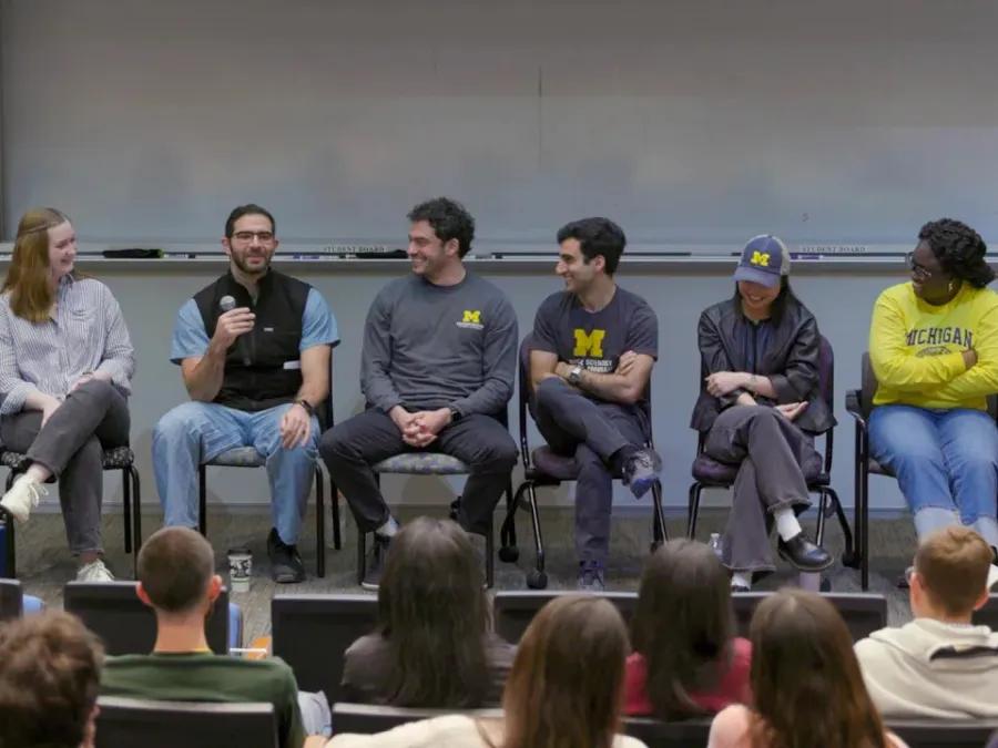 Six medical student sit on a panel on stage before an audience