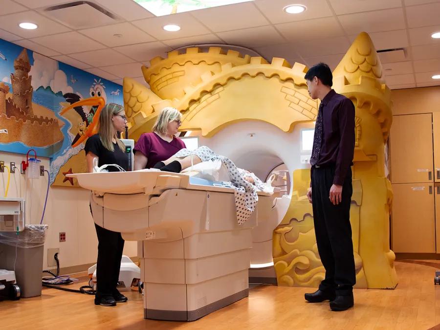 Pediatric radiology staff assisting a child with a scan in a room with colorful wall art