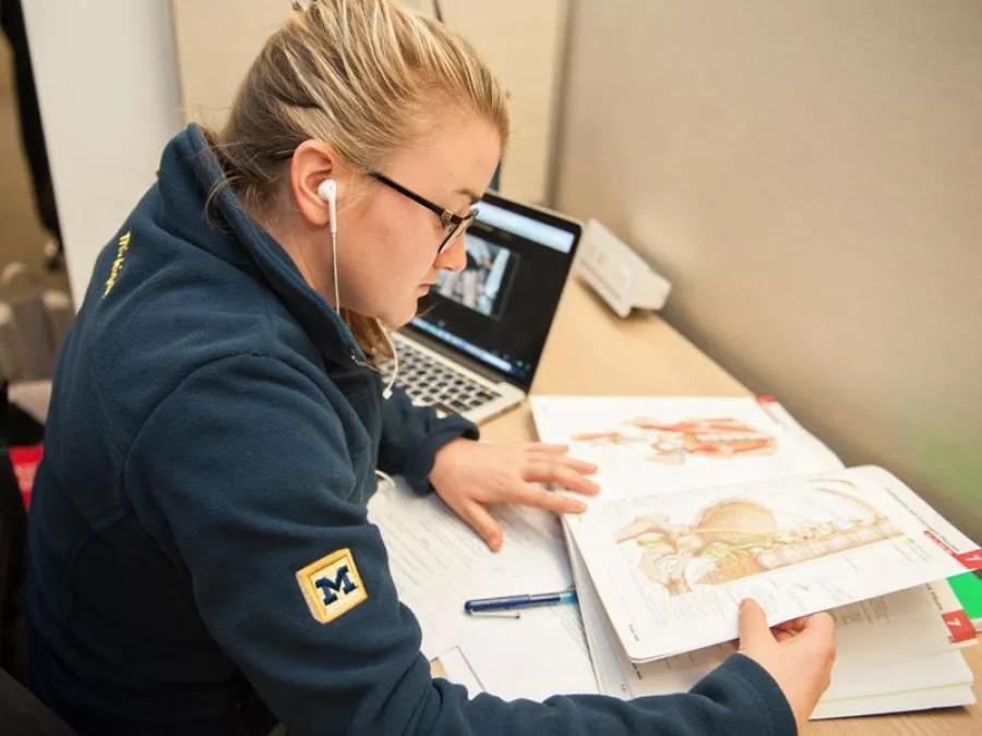 Student looking at anatomy book with laptop on the desk