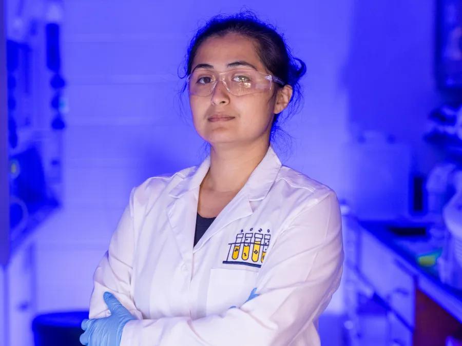 A researcher in a lab coat standing in a blue-lit laboratory.