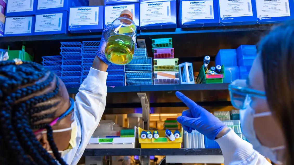 women in lab examining sample jar, one woman points at the sample 