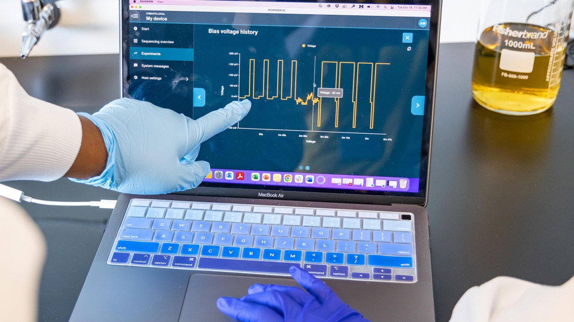 Hand protected by a blue latex glove points to a graph on a laptop screen.