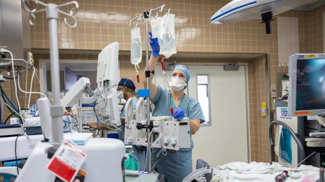 OR nurse reaches up to double check the IV bags for the patient surgery 