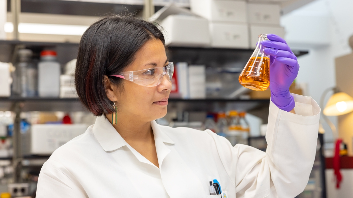 Researcher in Isom lab holds beaker full of liquids 