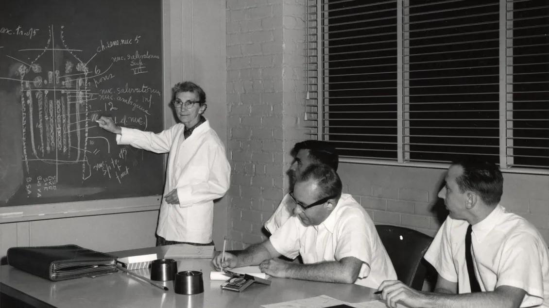  A black and white photo of a group of people at a table. 