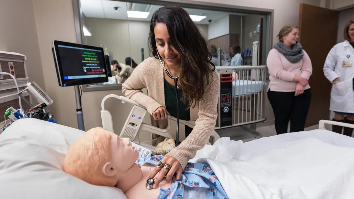 Three people practicing in a patient room on a patient dummy
