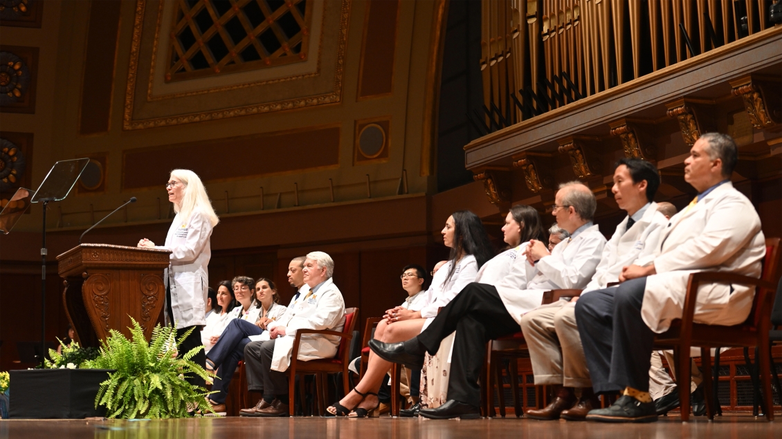 U-M Medical School faculty seated on stage at Hill Auditorium with Debra Weinstein speaking