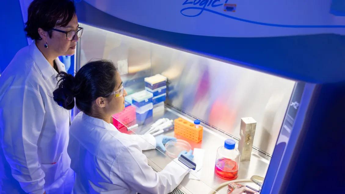 Two female researchers at a lit-up lab station with blue background