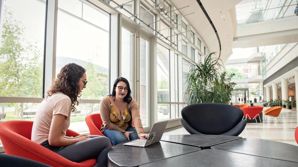 Two people sitting in a lobby working on a laptop