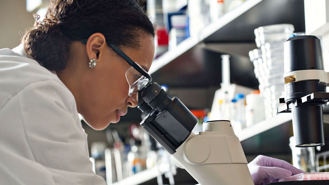 Scientist in lab coat examining specimen under microscope