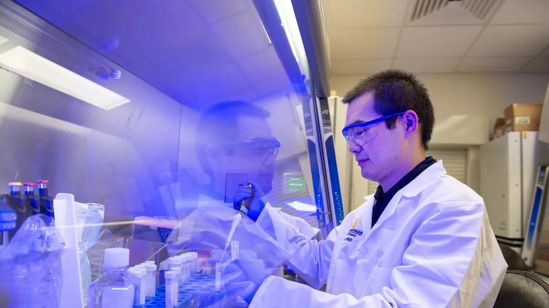 man standing in Zou lab using pipette to transfer liquids into test tube 