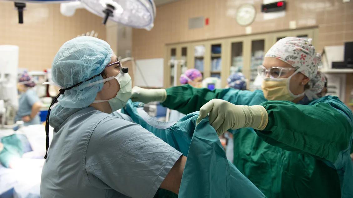 doctor in teal scubs holds up gown for the surgeon to scrub into to prepare for surgery 