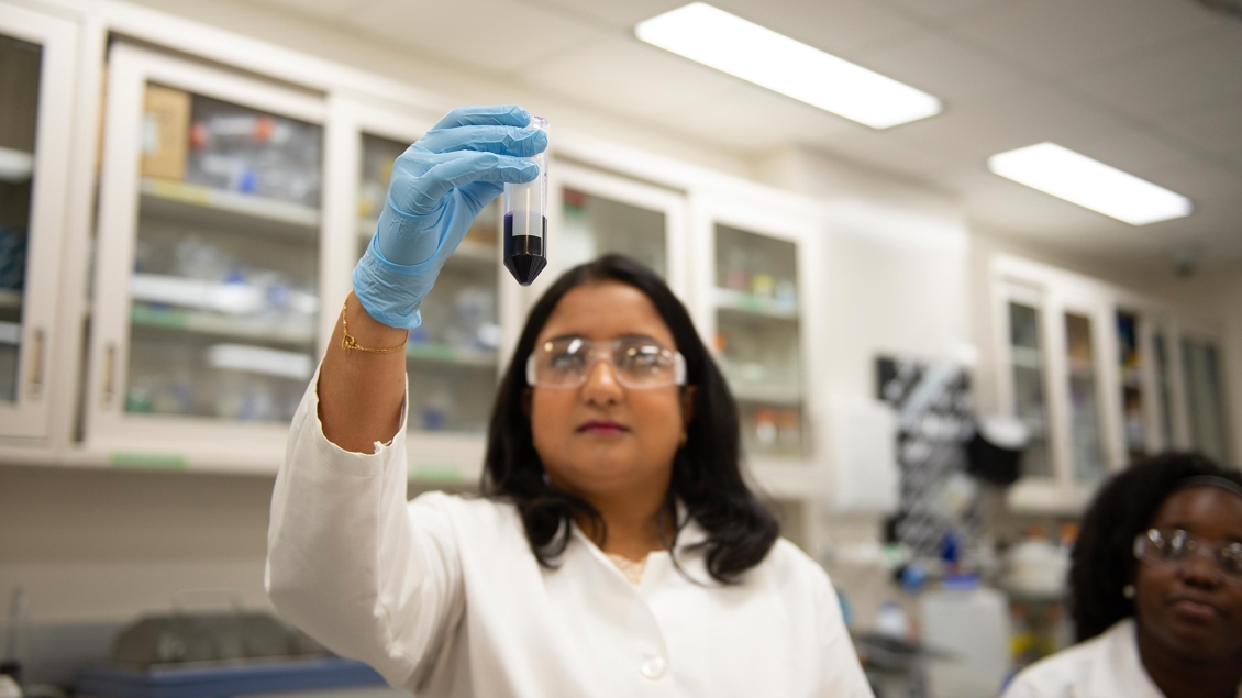 Woman in lab holding up test tube to light to look at sample 