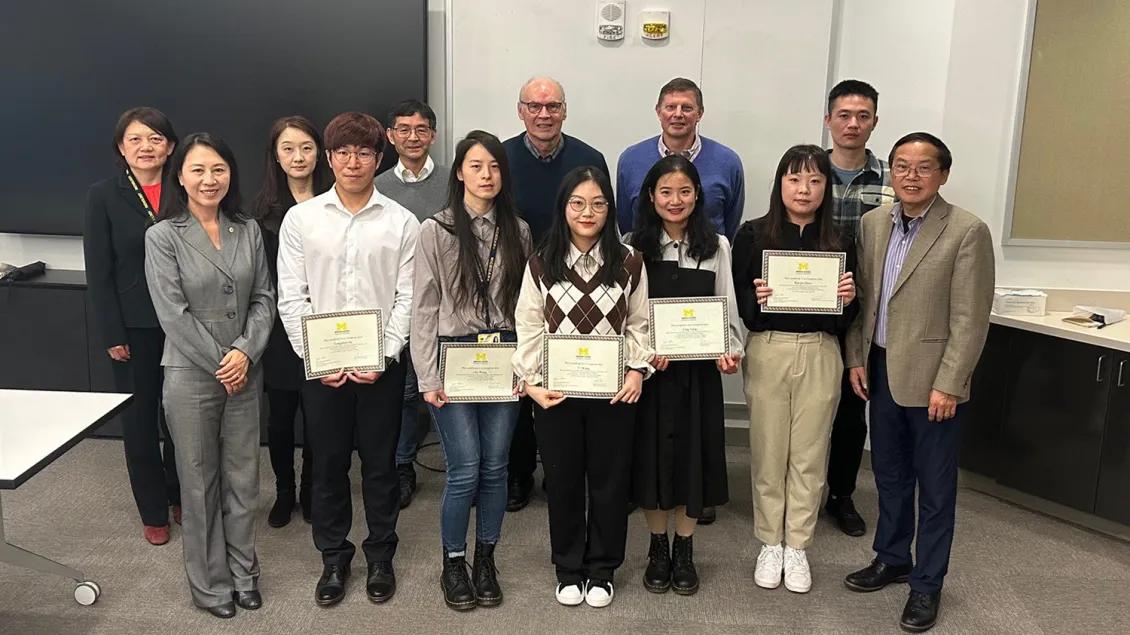 Group of people standing for a photo, some in the front row holding framed certificates
