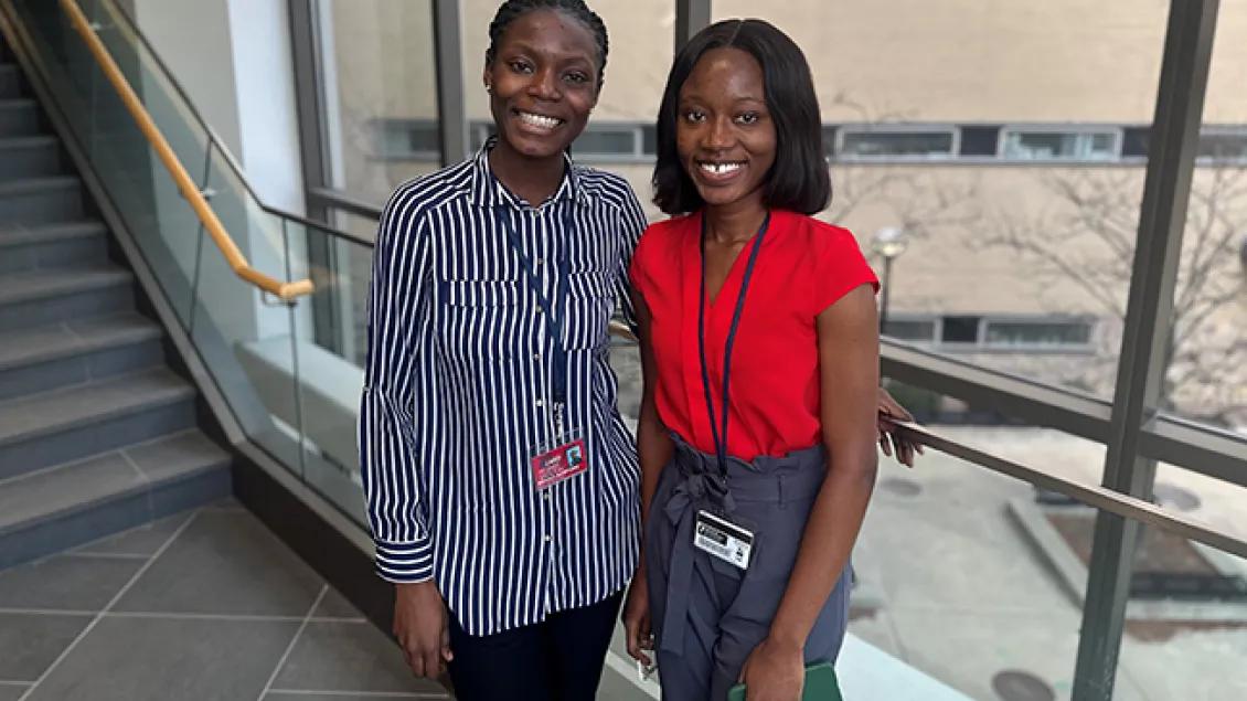 A woman wearing a blue and white striped blouse standing for a photo with another woman wearing an orange blouse and grey pants