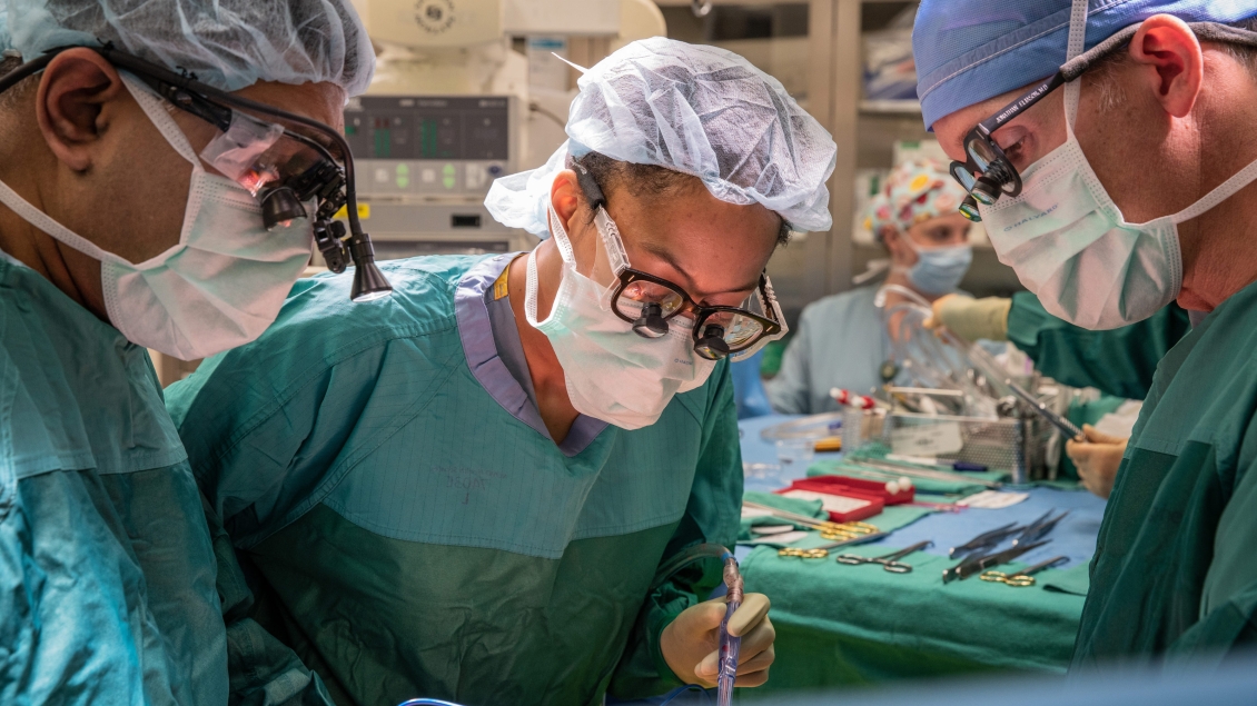 Three surgeons in green scrubs and surgical masks preparing for an operation.